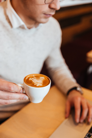 Cropped image of young man sitting in cafe while drinking coffee and using laptop.の写真素材