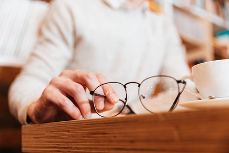 Cropped image of young man sitting in cafe. Focus on hands holding eyeglasses.の写真素材