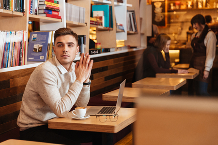 Photo of handsome young man sitting in cafe and chatting by laptop computer. Looking aside.の写真素材