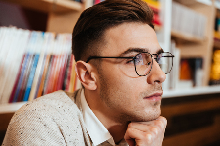 Image of concentrated young man wearing eyeglasses sitting in cafe while look aside.の写真素材