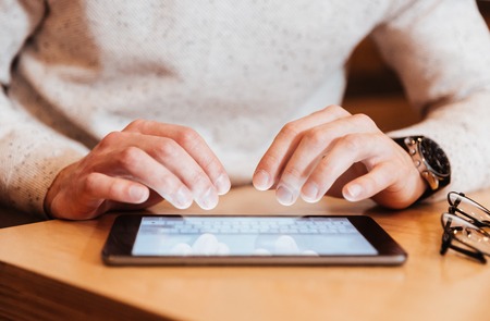 Cropped photo of young handsome man sitting in cafe while using tablet computer.の写真素材