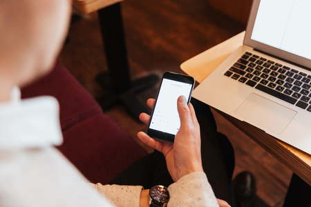 Cropped photo of young man sitting in cafe while using mobile phone and laptop computer.の写真素材