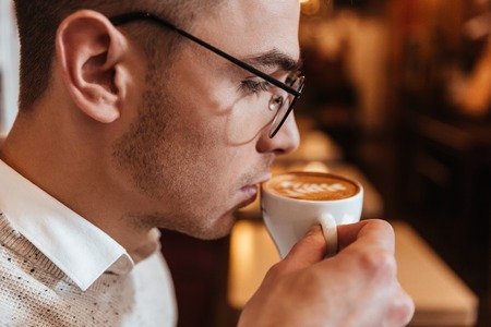 Picture of young attractive man sitting in cafe while drinking coffee and looking aside.の写真素材