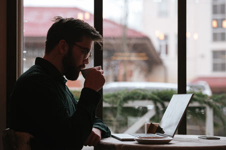 Photo of handsome bearded young man wearing glasses sitting in cafe and using laptop computer.の写真素材