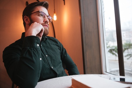Picture of handsome bearded young man wearing glasses sitting in cafe and look aside.の写真素材
