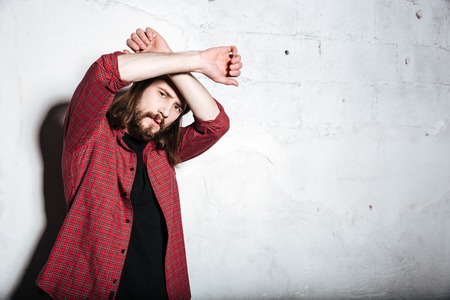 Photo of serious young bearded hipster man wearing hat dressed in shirt in a cage isolated over wall background looking at camera.の写真素材