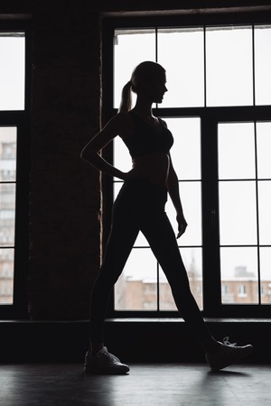 Silhouette of attractive young woman athlete standing near the windowの写真素材