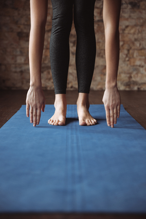 Closeup of slim young fitness woman standing barefoot and stretching on matの写真素材