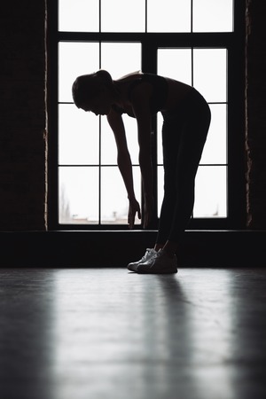Silhouette of pretty young fitness woman stretching near the windowの写真素材