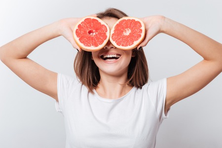 Picture of cheerful young lady standing over white background while holding grapefruitの写真素材