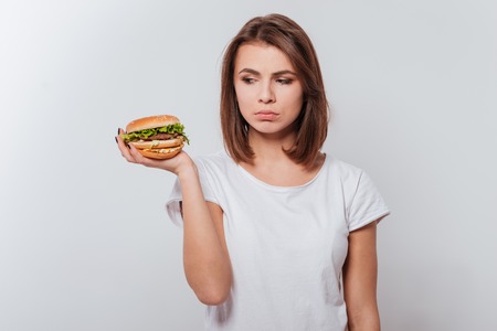 Photo of confused young lady standing over white background while holding fastfoodの写真素材