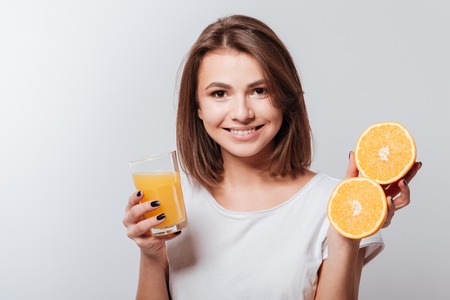 Photo of attractive young lady standing over white background while holding orange and juice