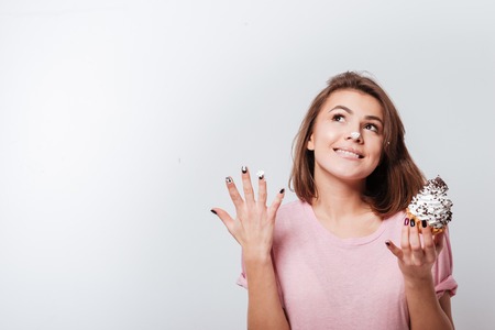 Photo of young cheerful woman standing over white background while eating cakeの写真素材