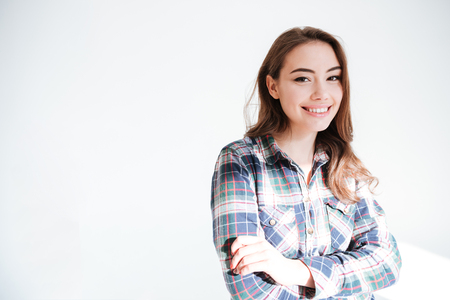 Cheerful pretty young woman standing with arms crossed over white backgroundの写真素材