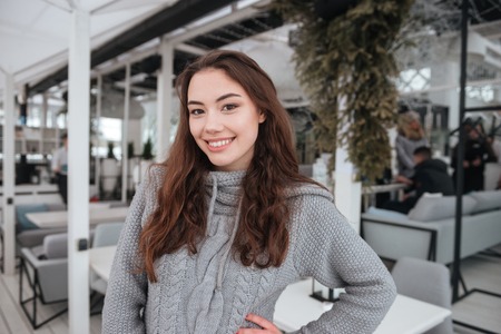 Photo of cheerful young lady dressed in sweater sitting in cafe at cold winter day. Look at camera.の写真素材