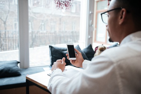 Back view picture of handsome african businessman wearing glasses sitting at the table chatting by phone. Coworking.の写真素材