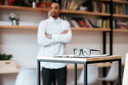 Image of african businessman standing in library. Focus on table with glasses.の写真素材