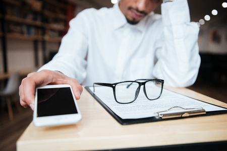 Cropped image of handsome african businessman sitting at the table holding phone. Coworking.の写真素材