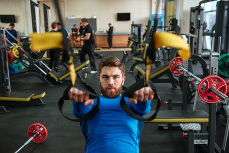 Photo of attractive young sportsman sitting in gym and make sport exercises.