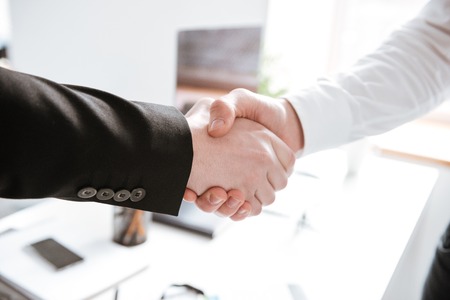 Cropped photo of handsome businessmen standing in office while shake their hands.の写真素材
