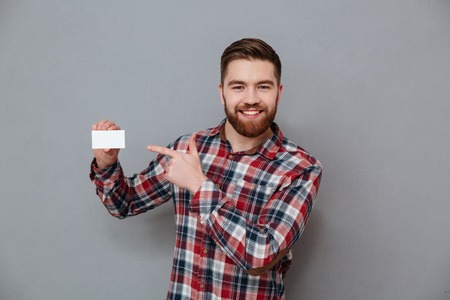 Photo of happy bearded man standing with copyspace business card and pointing on it.の写真素材