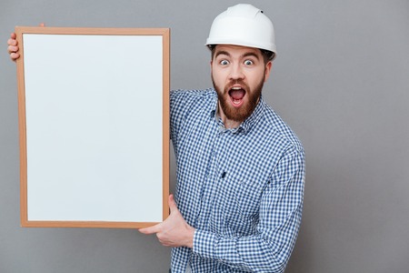 Photo of shocked builder holding copyspace board standing over grey background.の写真素材