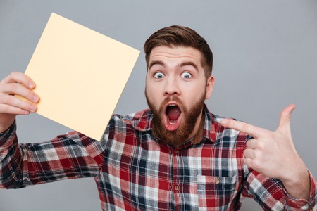 Picture of shocked bearded man holding copyspace blank standing over grey background and pointing.の写真素材