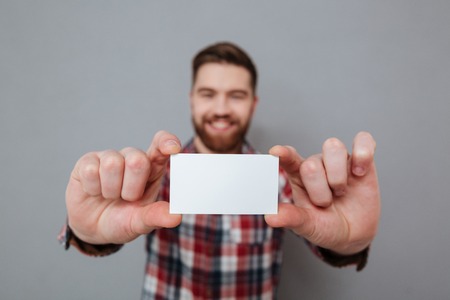 Image of attractive bearded man showing copyspace business card to camera. Focus on card.の写真素材