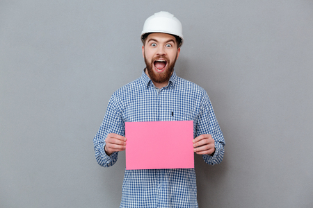 Picture of happy bearded man builder holding copyspace blank standing over grey background.の写真素材