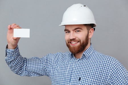Image of happy bearded builder holding copyspace business card standing over grey background.の写真素材