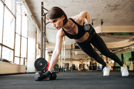 Attractive young woman athlete doing exercises with dumbbells in gymの写真素材
