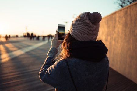 Back view of a young girl in hat taking picture of a sea pier view