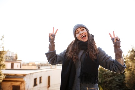 Cheerful young woman standing and showing peace sign in the cityの写真素材