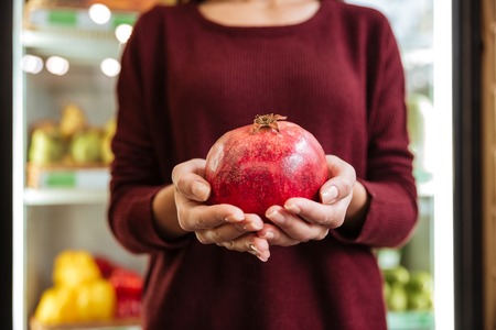 Closeup of woman standing and holding pomegranate at grocery storeの写真素材