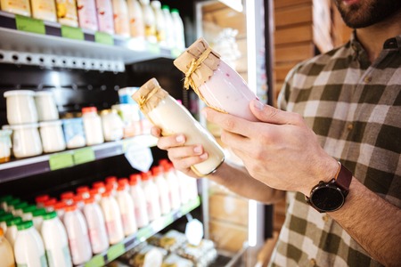 Closeup of man standing and buying yoghurt in bottles at grocery shopの写真素材