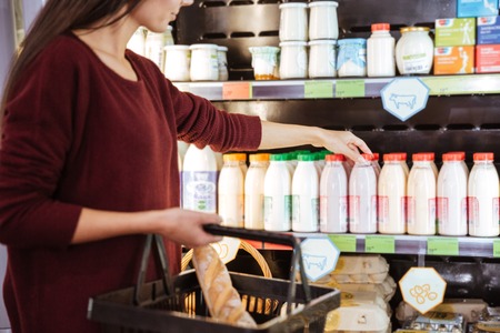 Closeup of woman with basket choosing and buying yoghurt in supermarketの写真素材