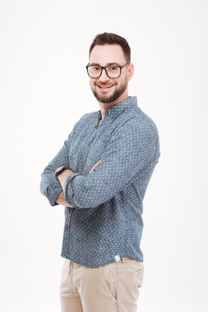 Picture of smiling young bearded man dressed in blue shirt wearing glasses posing isolated over white background.の写真素材