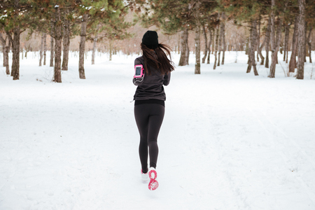 Back view of young fitness woman running in a city park in winterの写真素材