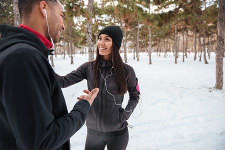 Smiling young couple talking while having break after jogging in winter forestの写真素材