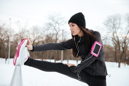 Close up portrait of a young fitness woman with armband stretching legs before running outdoors