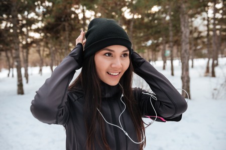 Portrait of a smiling fitness woman in earphones jogging outdoors in winterの写真素材