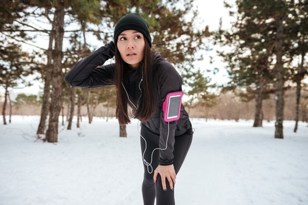 Woman jogging in snowy city park with earphones and armbandの写真素材