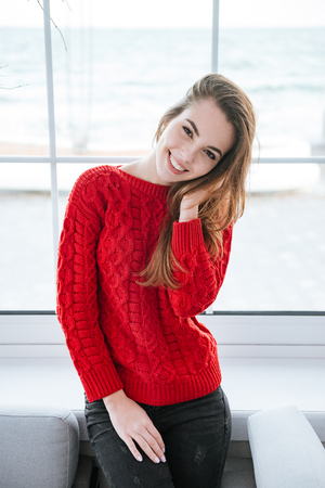 Photo of cheerful young lady standing in cafe at cold winter day and posing. Look at camera.の写真素材