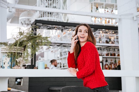 Picture of smiling young woman sitting in cafe at cold winter day and talking by phone.の写真素材