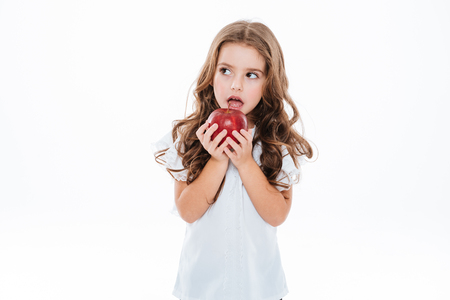 Pensive worried little girl standing and holding red apple over white backgroundの写真素材