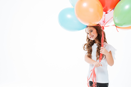 Smiling cute little girl standing and holding colorful balloons over white backgroundの写真素材