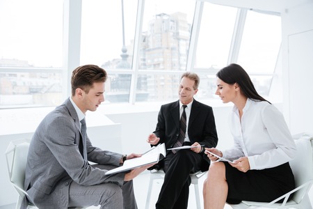 Three business people sit on chairs with documents in conference roomの写真素材