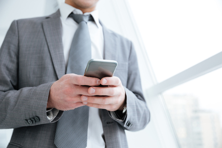 Cropped image of business man using phone and standing near the windowの写真素材