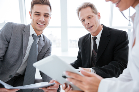 Cropped image of three business people sit with tablet computer in office. Focus on tabletの写真素材