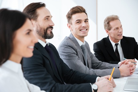 Side view of Happy Business people sit by the table in office and one man looking at cameraの写真素材